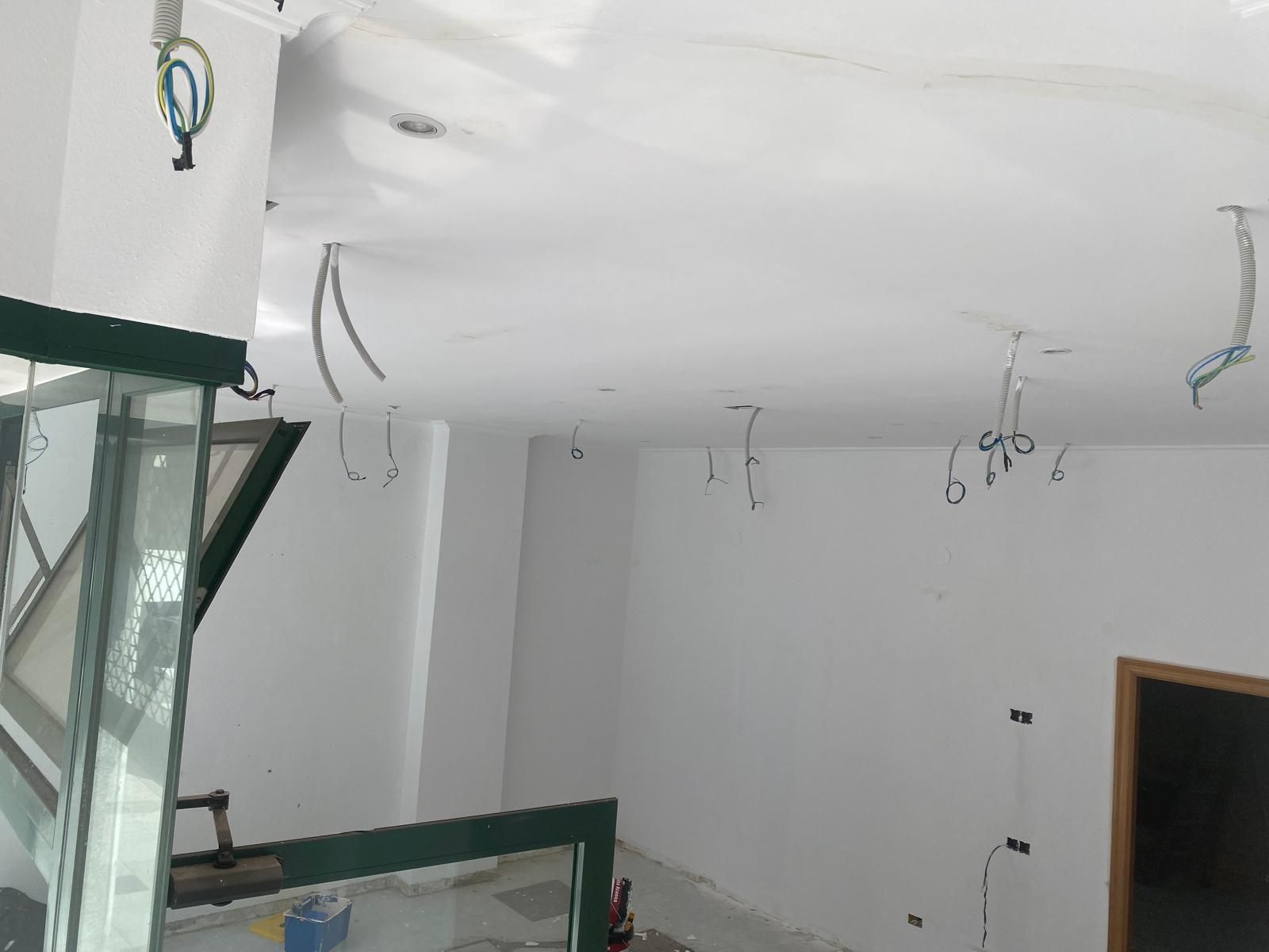 Zona de construcción con techo blanco, cables expuestos, andamios verdes y una puerta abierta.