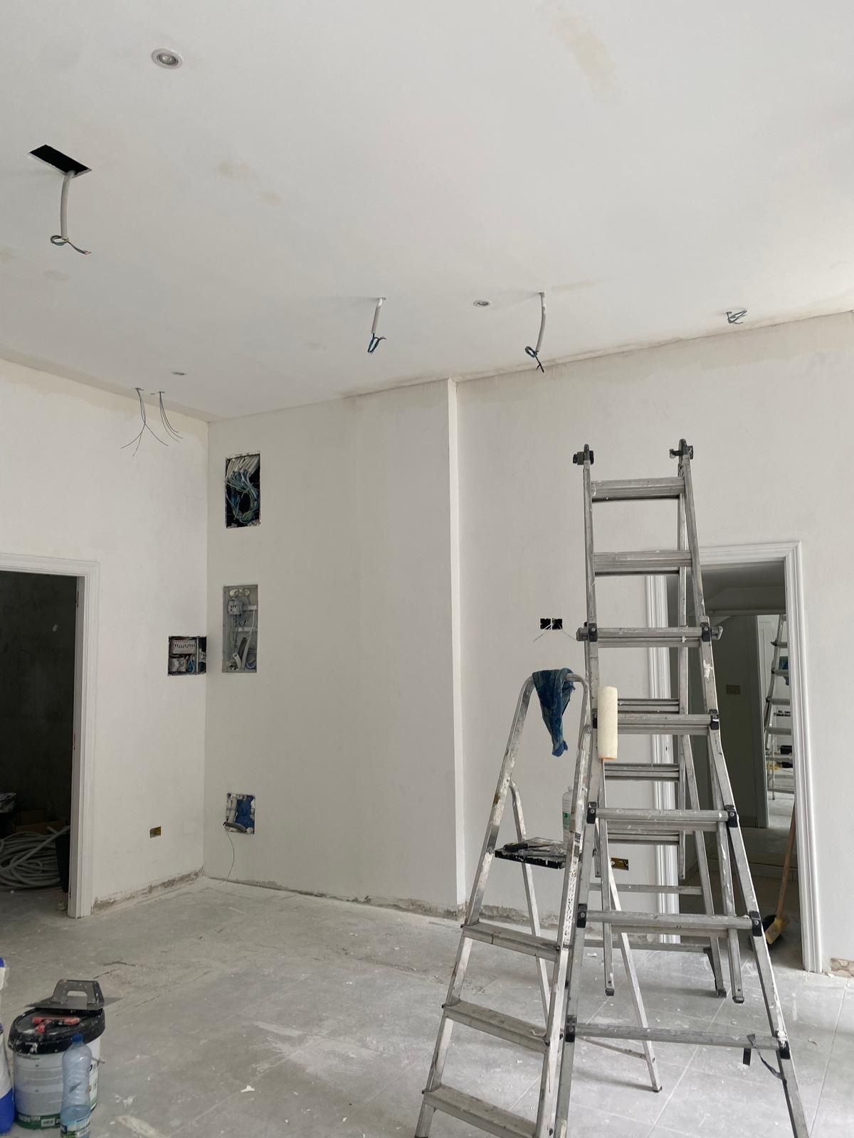 Habitación parcialmente reformada con escaleras, herramientas y paredes y techo blancos sin terminar.