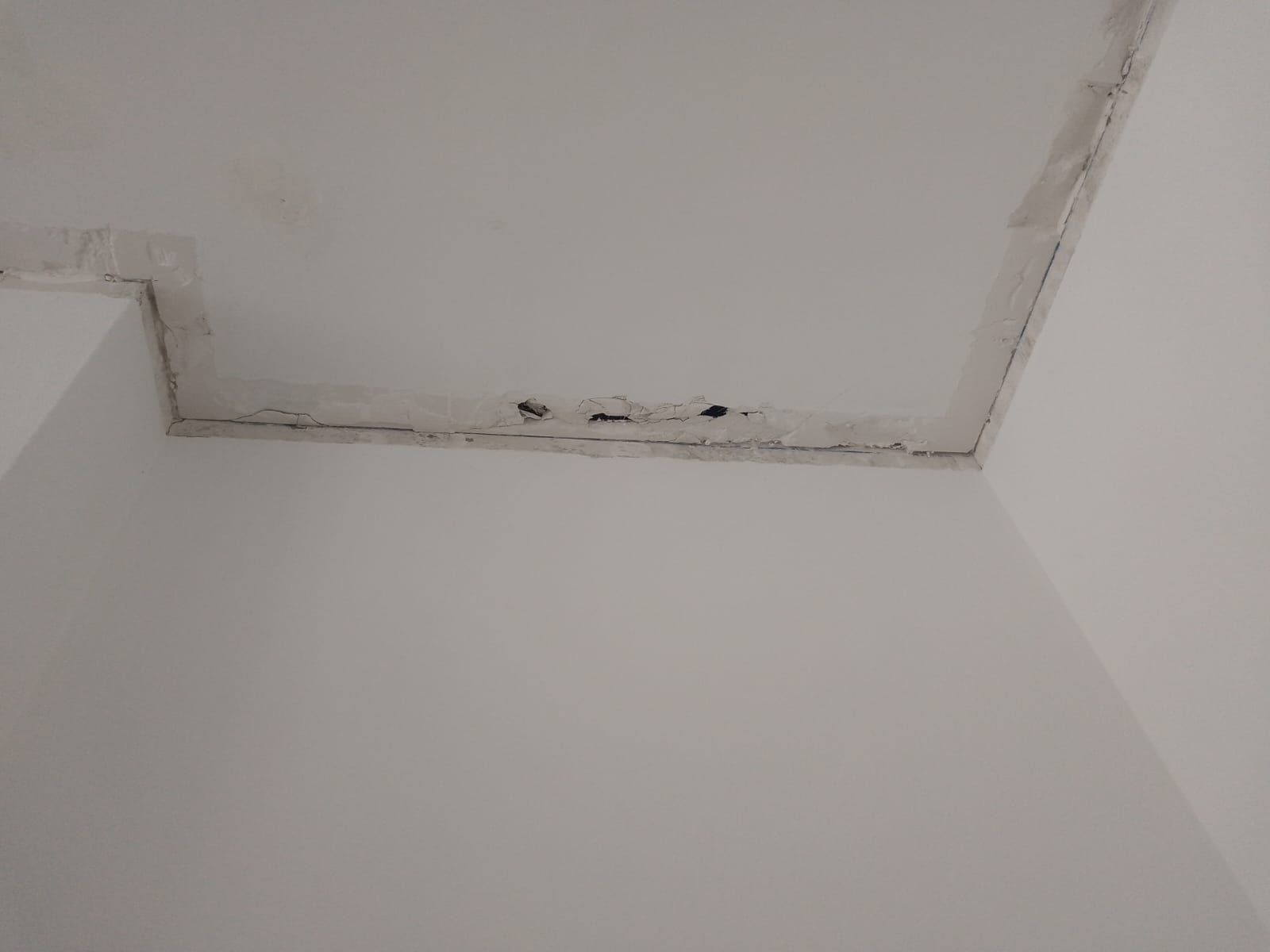 Esquina del techo dañada con pintura descascarada y manchas oscuras de agua en las paredes blancas.