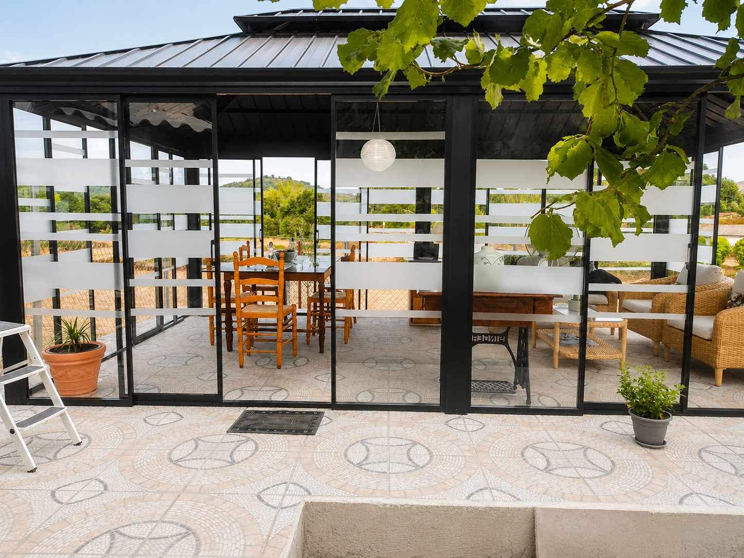 Cafetería moderna con patio, paredes de cristal, mesas de madera, techo negro y plantas en macetas.