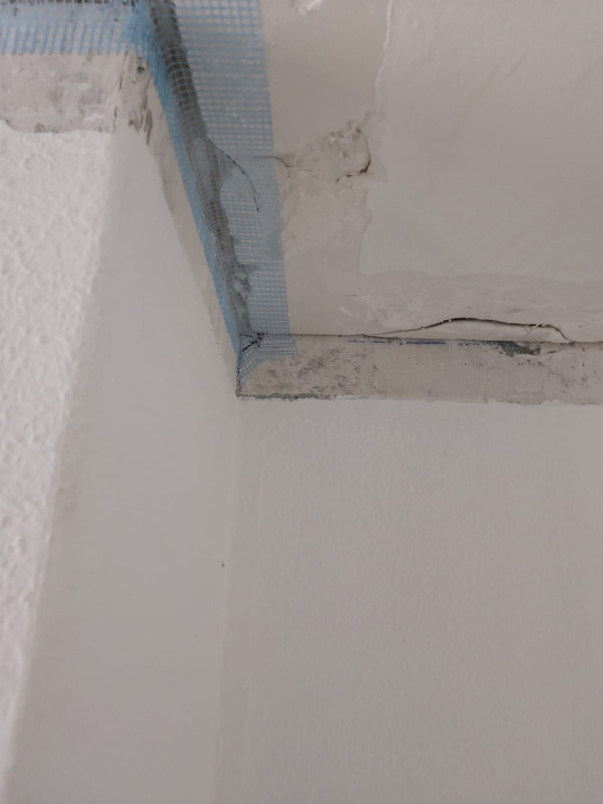Esquina del techo de una habitación con grietas visibles, pintura descascarada y cinta adhesiva azul para reparaciones.