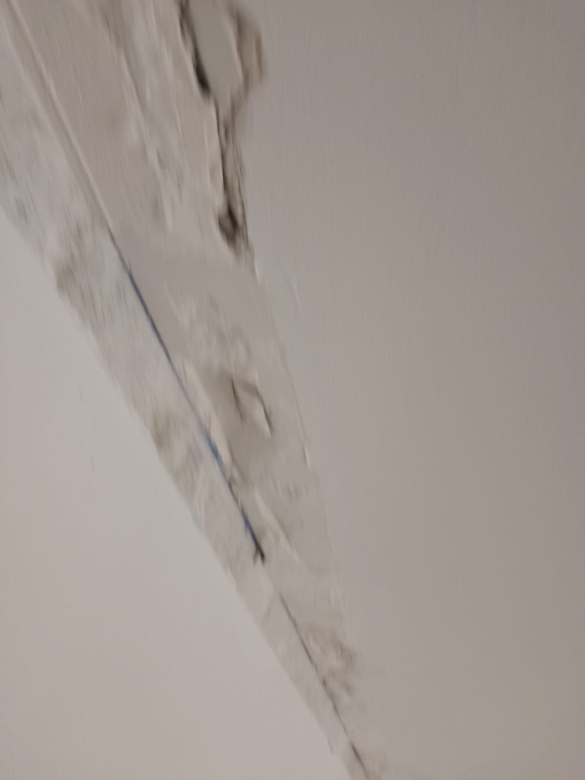 Pared blanca dañada con pintura descascarada y yeso agrietado a lo largo de una junta de esquina.