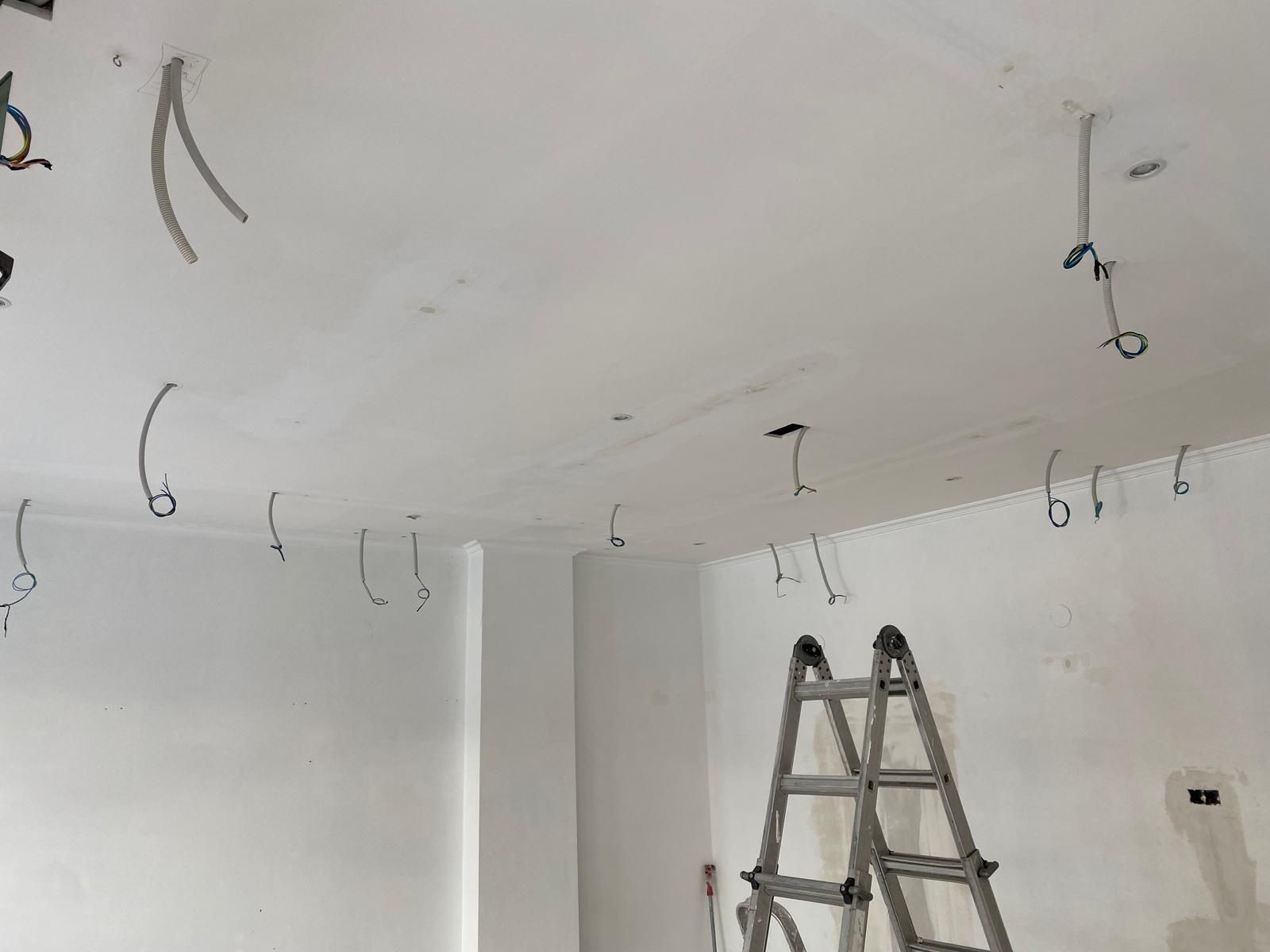 Escalera en una habitación blanca con ganchos en el techo y cables colgantes durante la renovación.