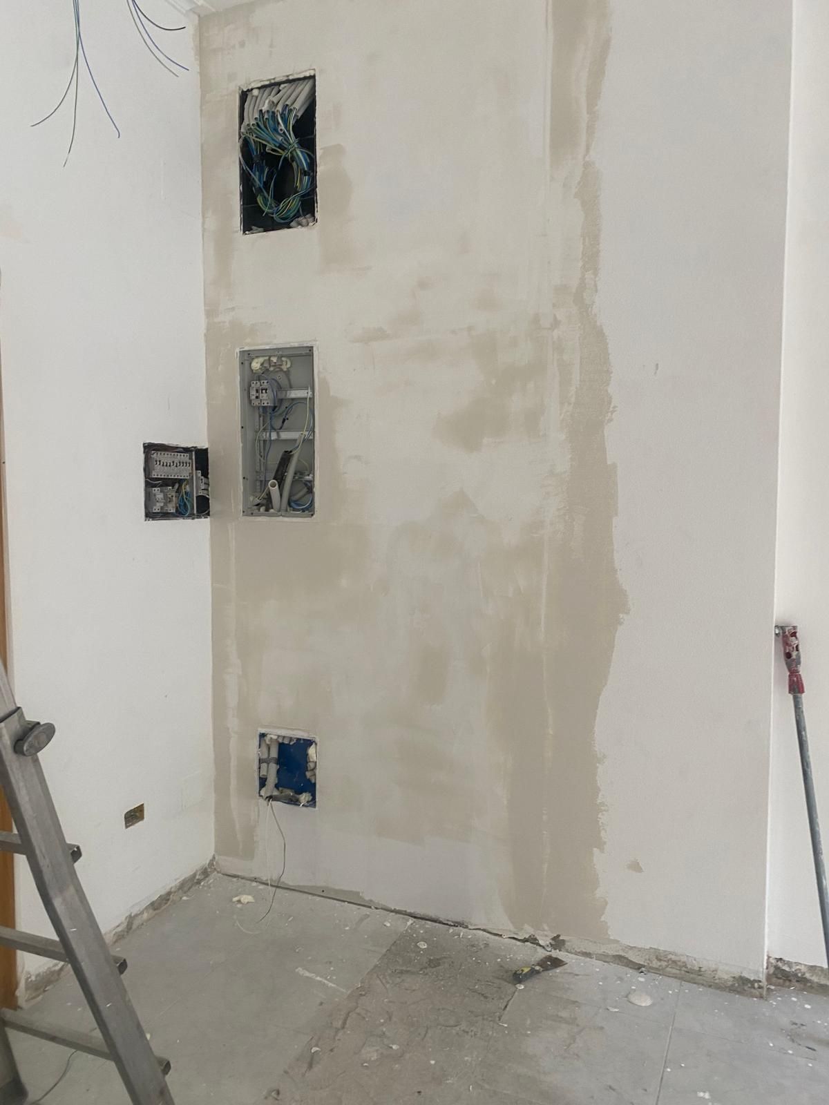 Pared interior parcialmente enlucida con cajas eléctricas y una escalera en una habitación en reforma.