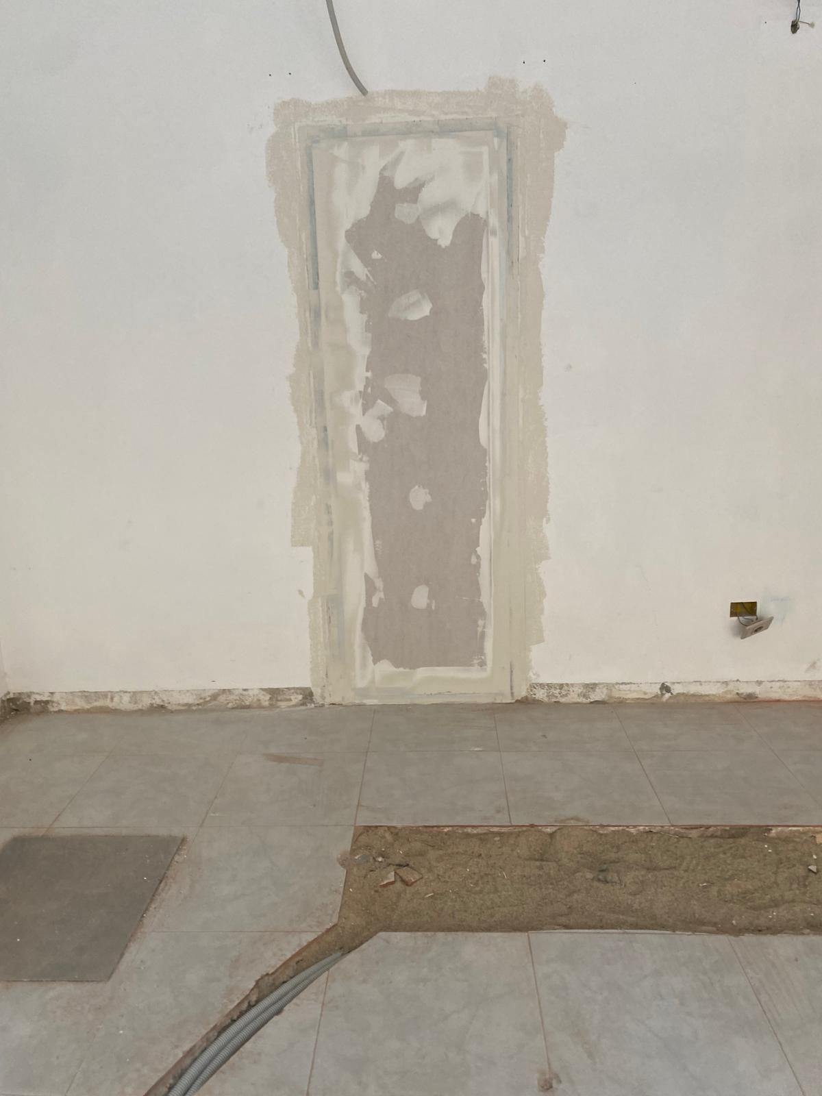 Estrecha franja de pladur sin terminar en una pared blanca sobre un suelo de hormigón.