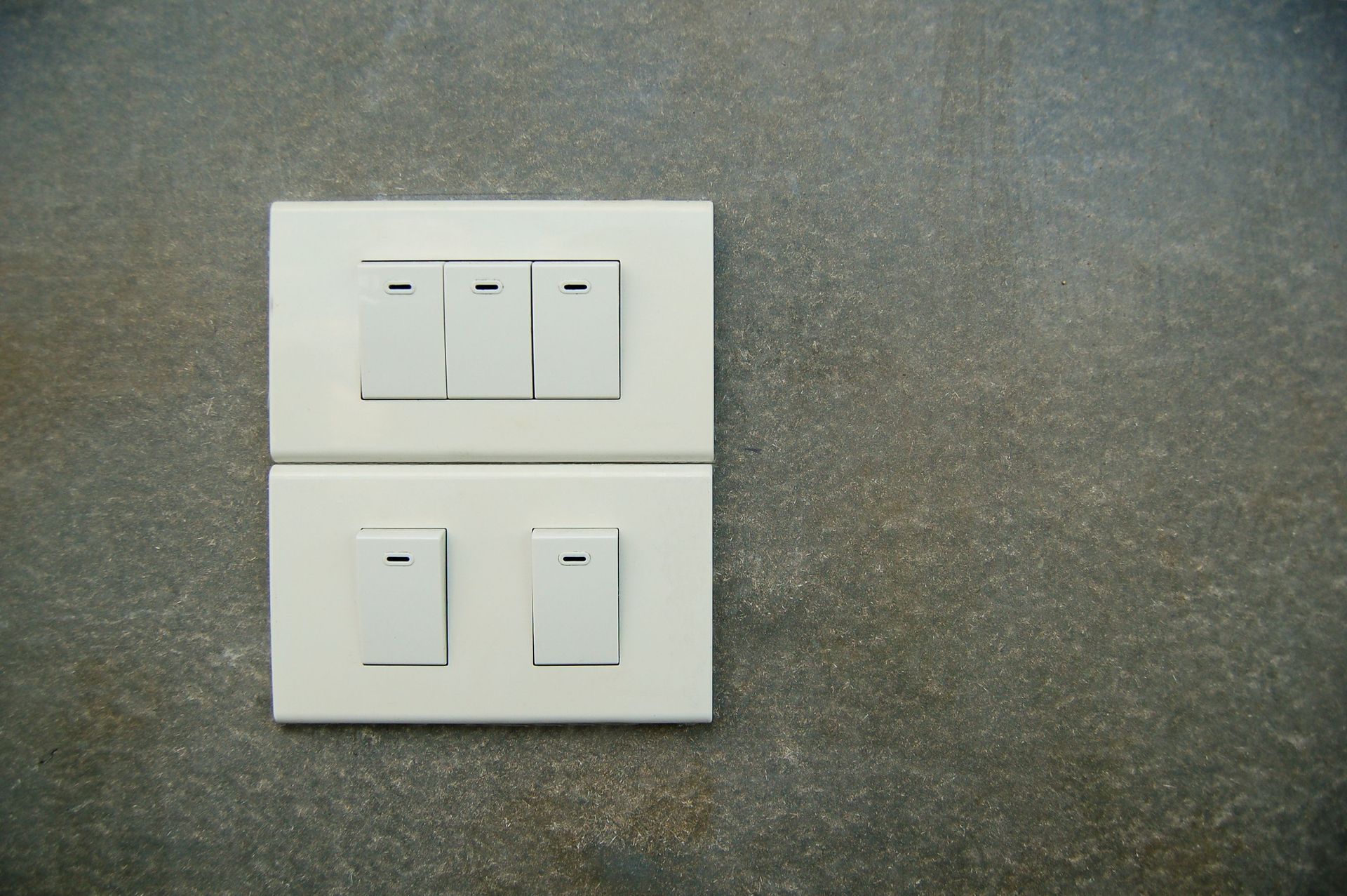 Placa de interruptor de pared blanca con tres interruptores encima de dos interruptores sobre una pared gris.