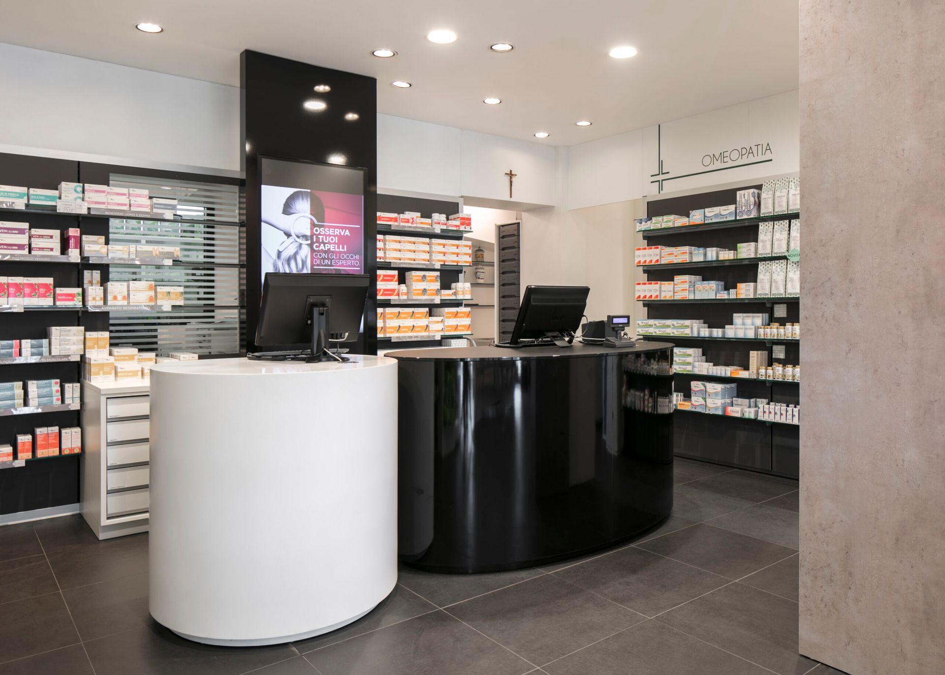 Interno di farmacia con bancone curvo bianco e nero, scaffali con medicinali e un computer.