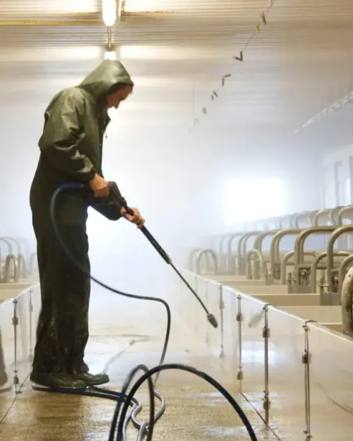 Persona que viste equipo impermeable lavando a presión una instalación industrial.