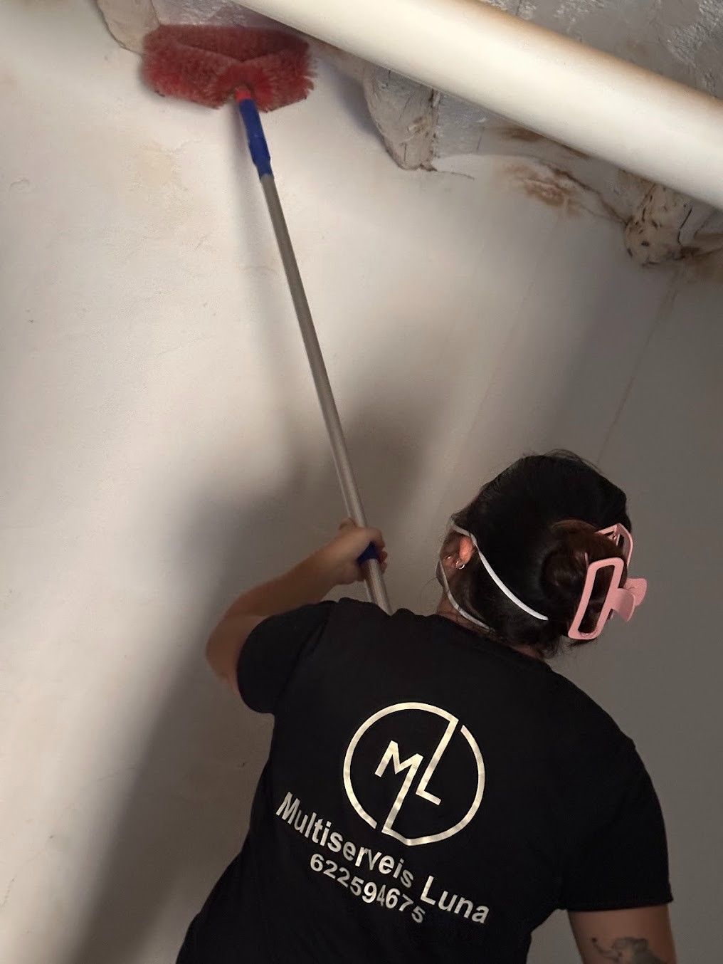 Persona limpiando un techo con un cepillo de mango largo; pared blanca y tubería visibles.