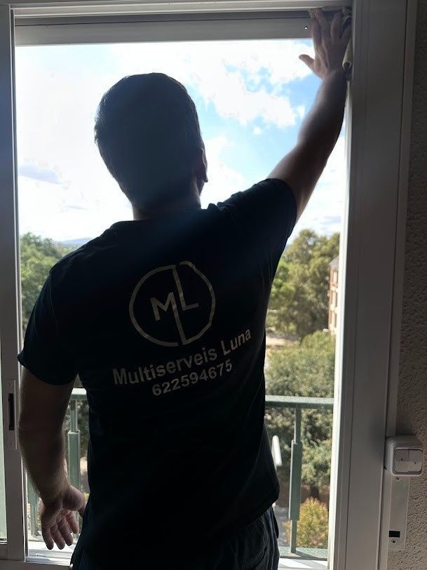 Persona arreglando una ventana; vista trasera. Vista exterior, con cielo azul. La camiseta tiene el logotipo