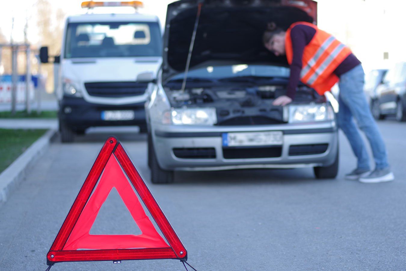 Triangle de signalisation devant un homme avec un gilet orange en train d'intervenir sur le moteur d'une voiture