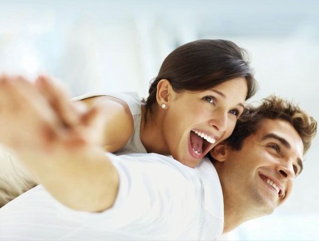 Un hombre lleva a una mujer en su espalda y están sonriendo.