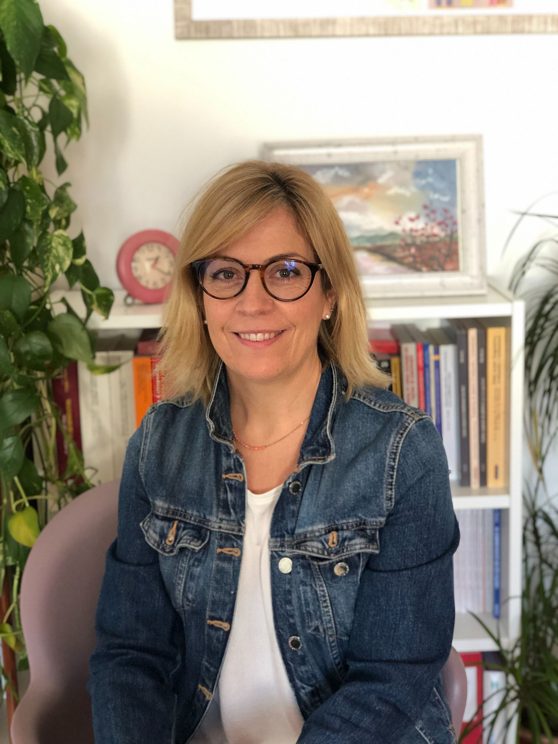 Una mujer que lleva gafas y una chaqueta vaquera está sentada en una silla.