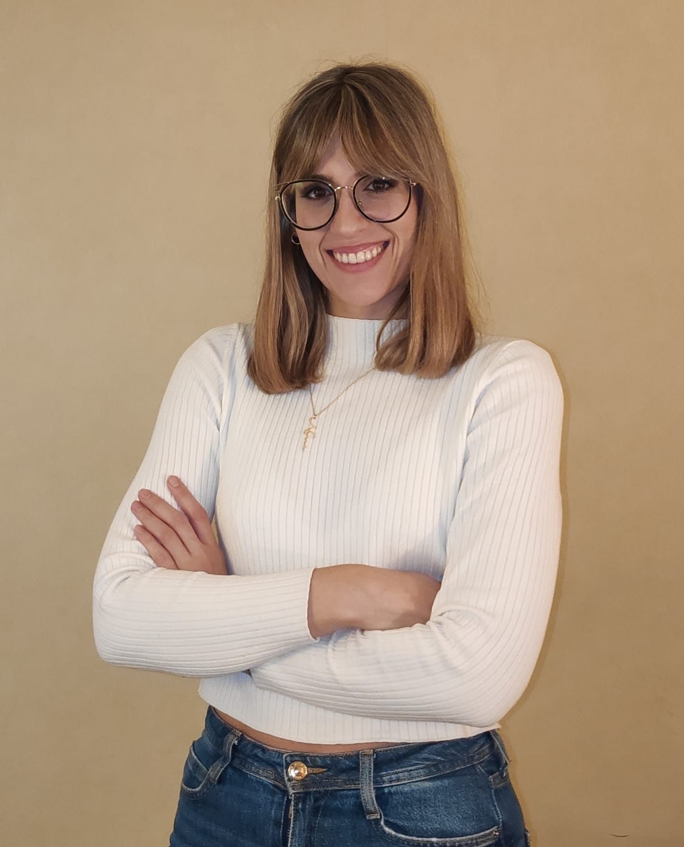 Una mujer que lleva gafas y un suéter blanco está de pie con los brazos cruzados.
