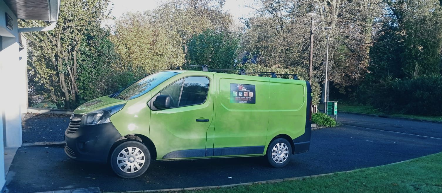 Camionnette verte garée dans une allée à côté d'un bâtiment, entourée de verdure.