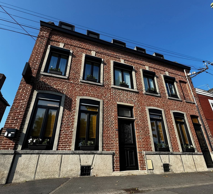 Maison en briques rouges avec fenêtres et porte à cadre noir, sur fond de ciel bleu.