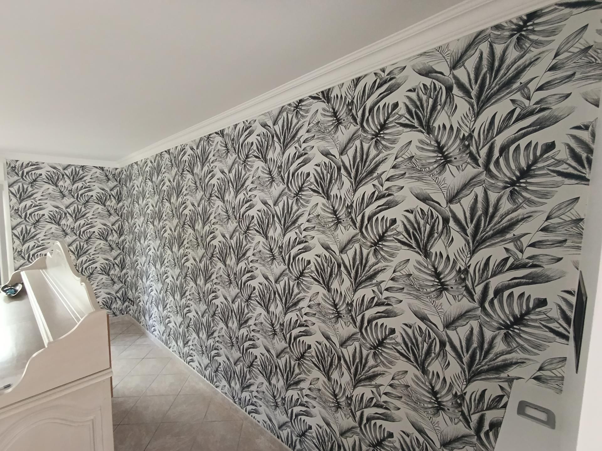 Chambre avec moulures blanches et murs recouverts de papier peint à feuilles tropicales noir et blanc.