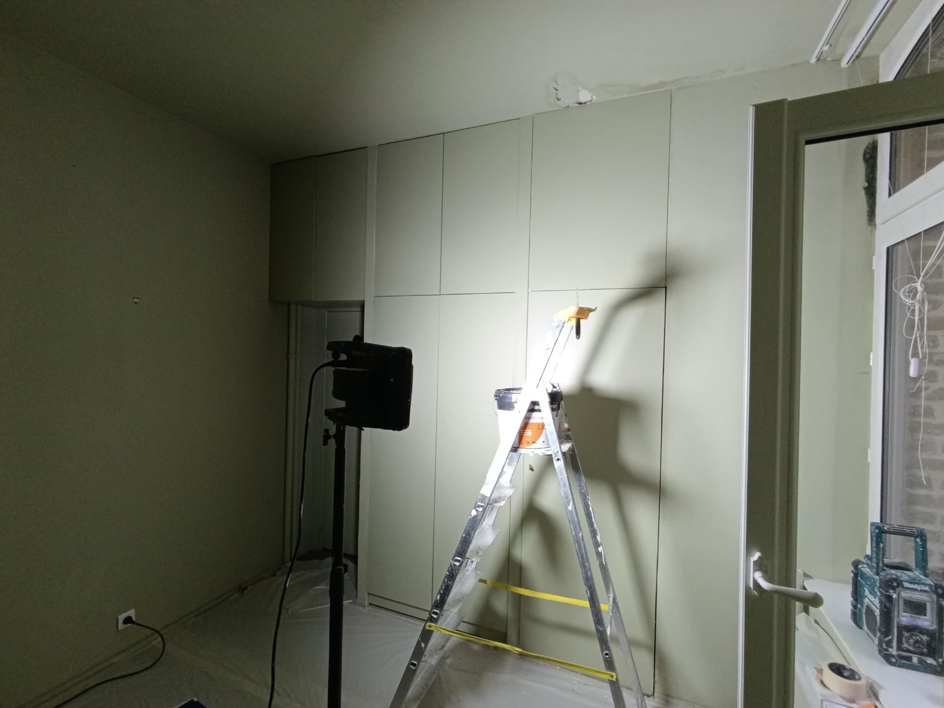 Intérieur de la pièce avec échelle et travaux de cloisons sèches en cours, murs verts.