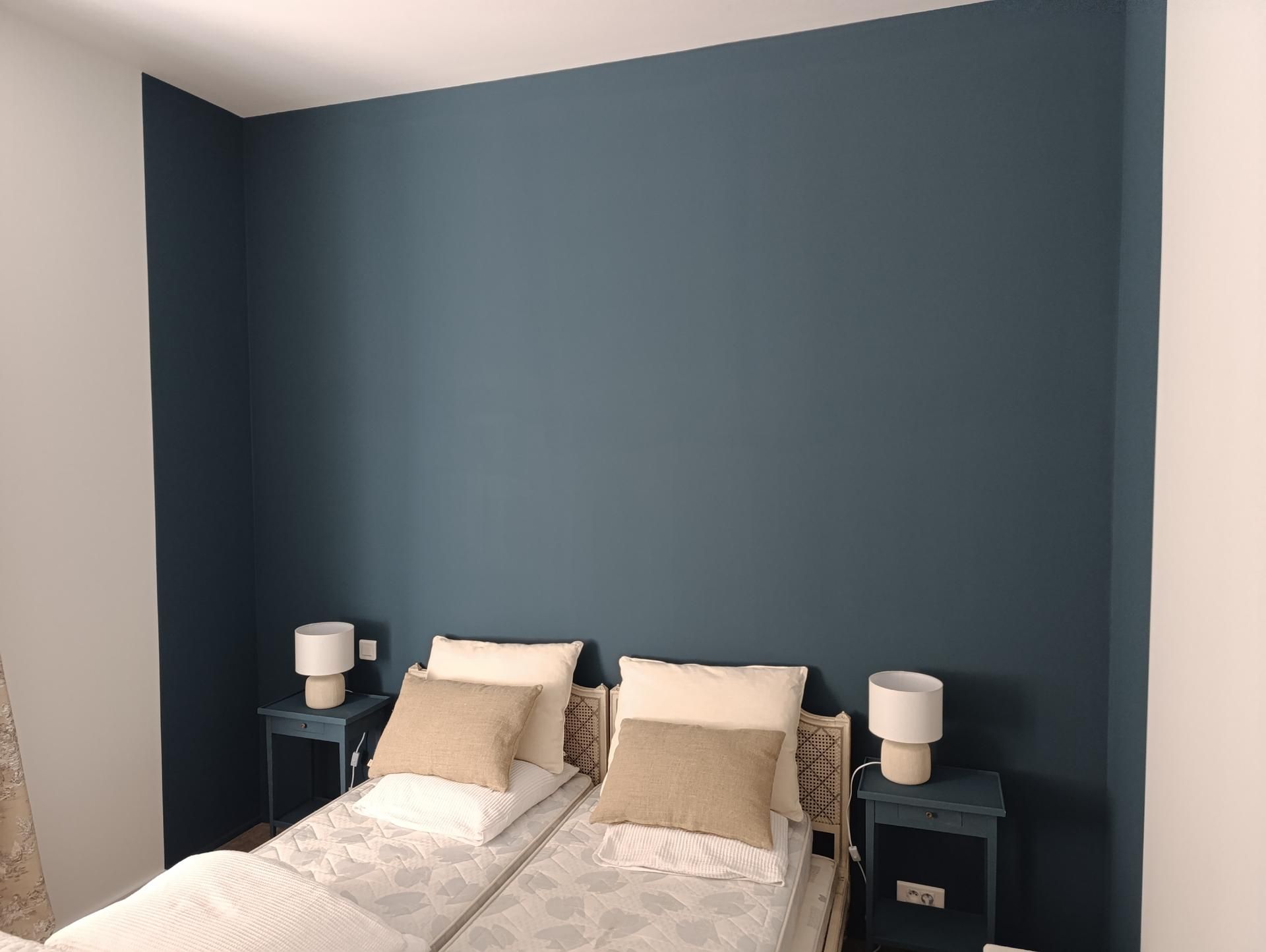 Deux lits jumeaux avec des oreillers beiges et des lampes sur des tables de nuit bleues contre un mur bleu sarcelle.