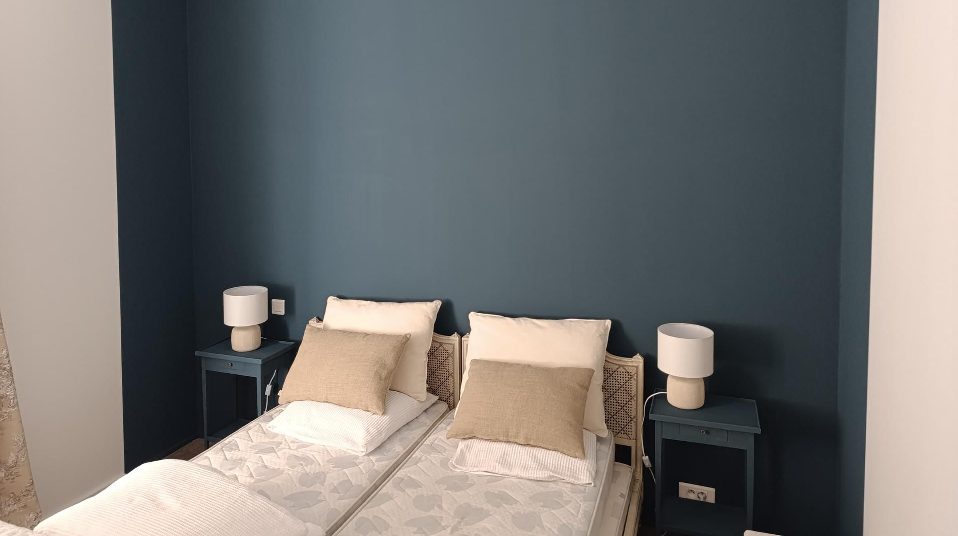 Lits jumeaux avec draps couleur crème, oreillers beiges et mur bleu à l'arrière.