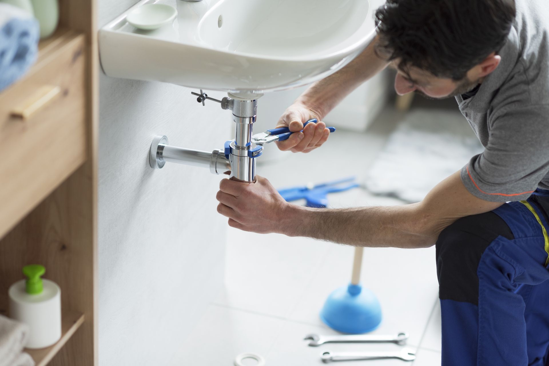 Plombier dans une salle de bains, travaillant sur les tuyaux d'un évier avec une clé.