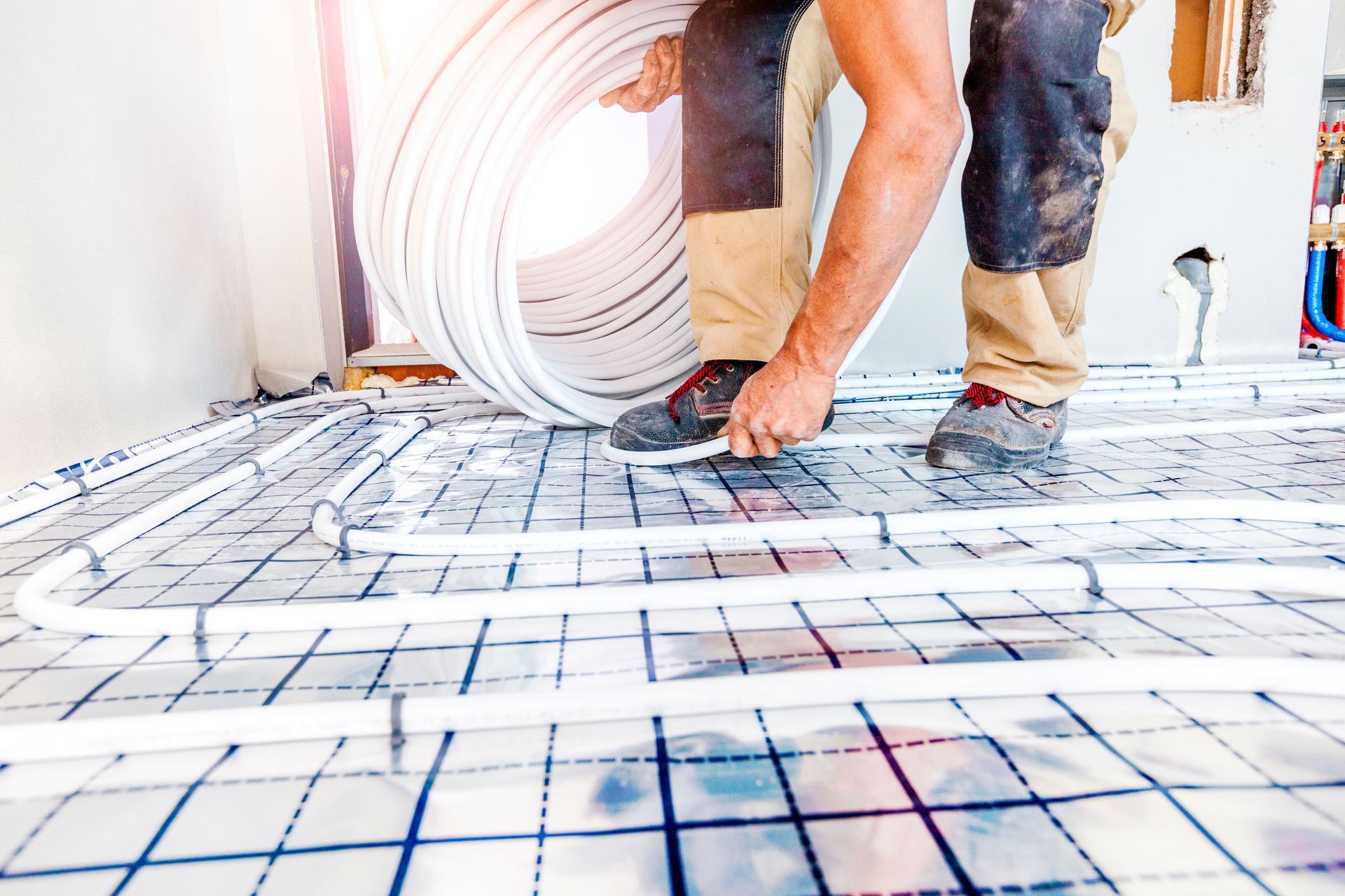 Un ouvrier installe un plancher chauffant, disposant des tubes blancs sur une grille bleue.