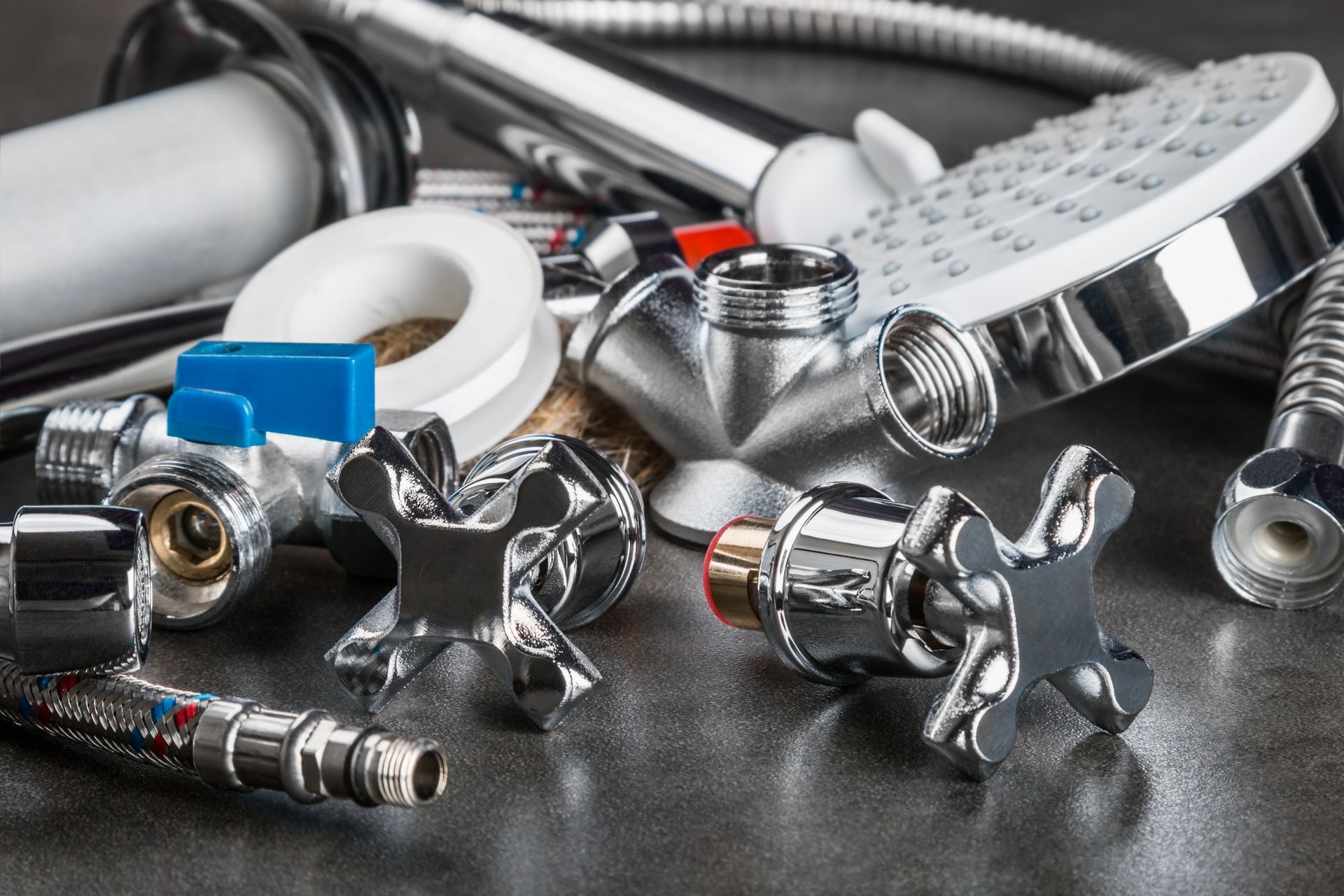 Appareils et pièces de plomberie au fini chromé, y compris pommeau de douche, robinets et valve, sur une surface sombre.