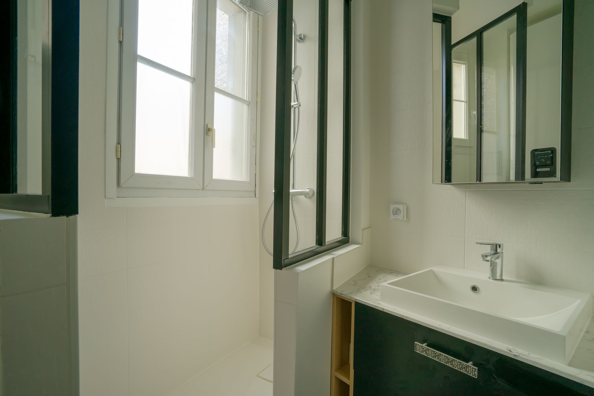 Petite salle de bains avec murs blancs, une fenêtre, une vanité et un miroir.