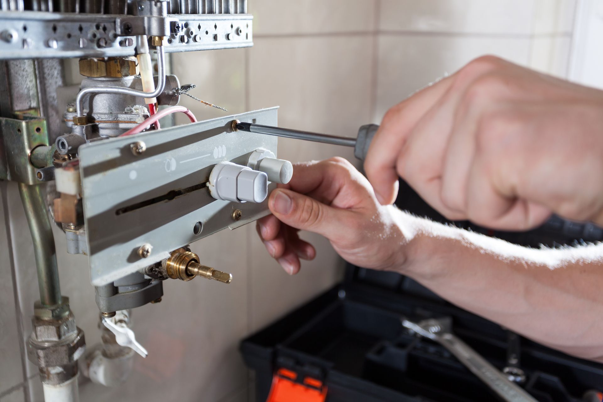 Personne utilisant un tournevis sur un chauffe-eau avec une boîte à outils à proximité.
