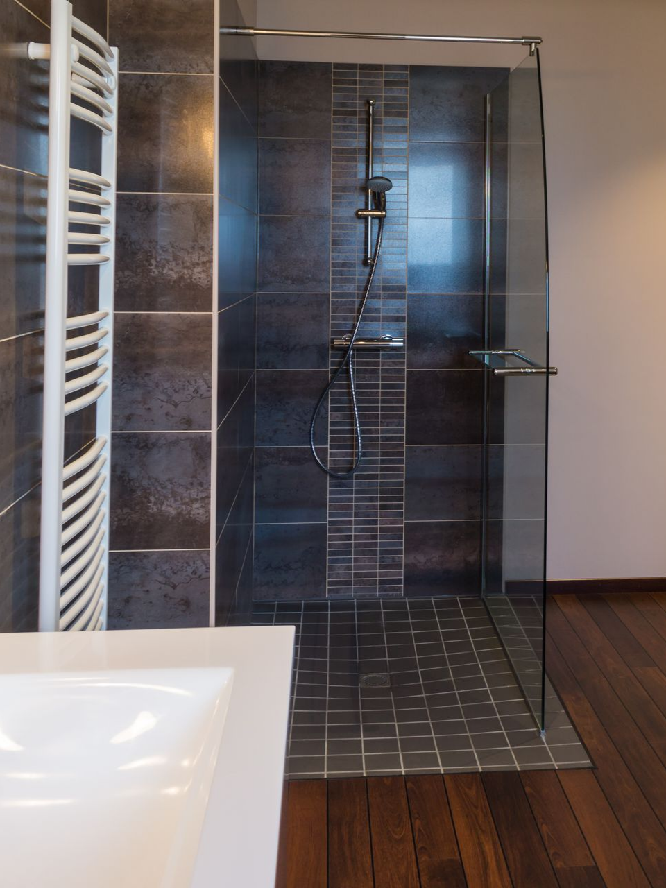 Douche moderne avec carrelage marron foncé, porte vitrée et porte-serviettes blanc.