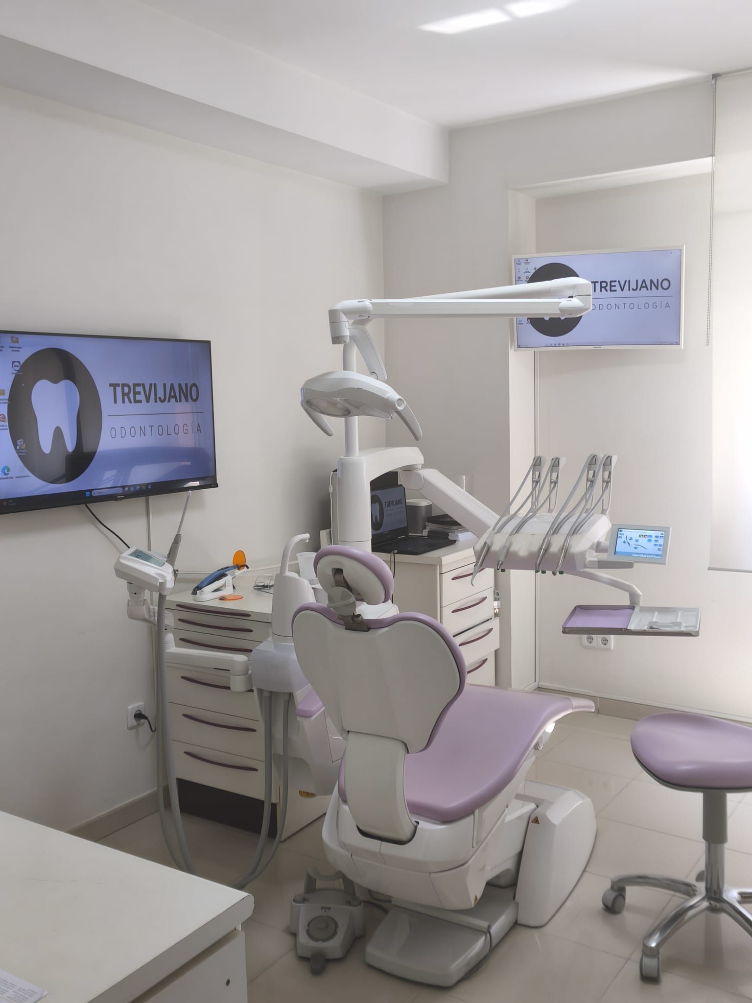 Clínica dental moderna con sillón, pantalla de rayos X y equipo dental en una sala blanca y limpia.