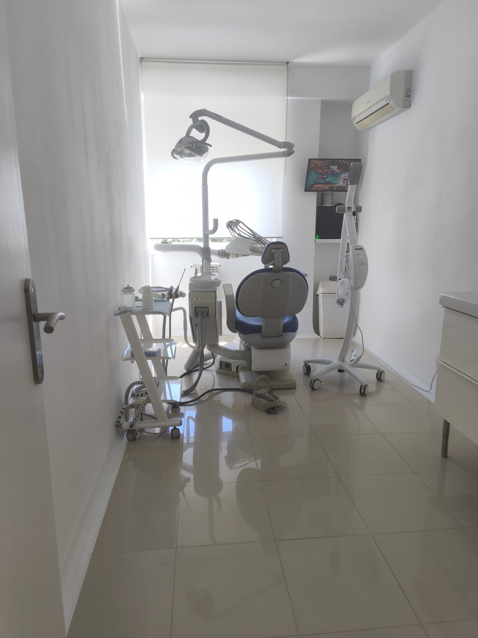 Sala de exploración dental luminosa con sillón, luz cenital y equipo médico sobre un suelo de baldosas brillantes.