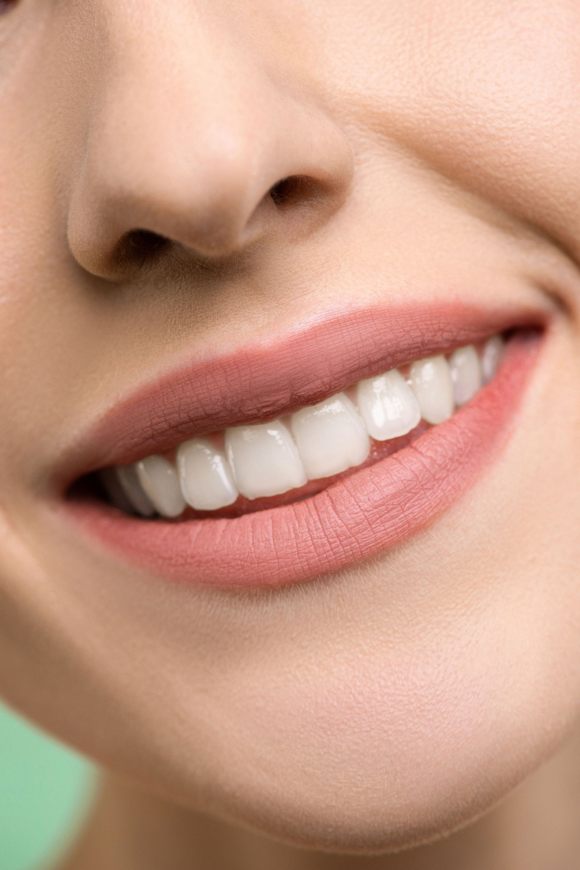 Primer plano de una boca sonriente con lápiz labial rosa y dientes blancos.