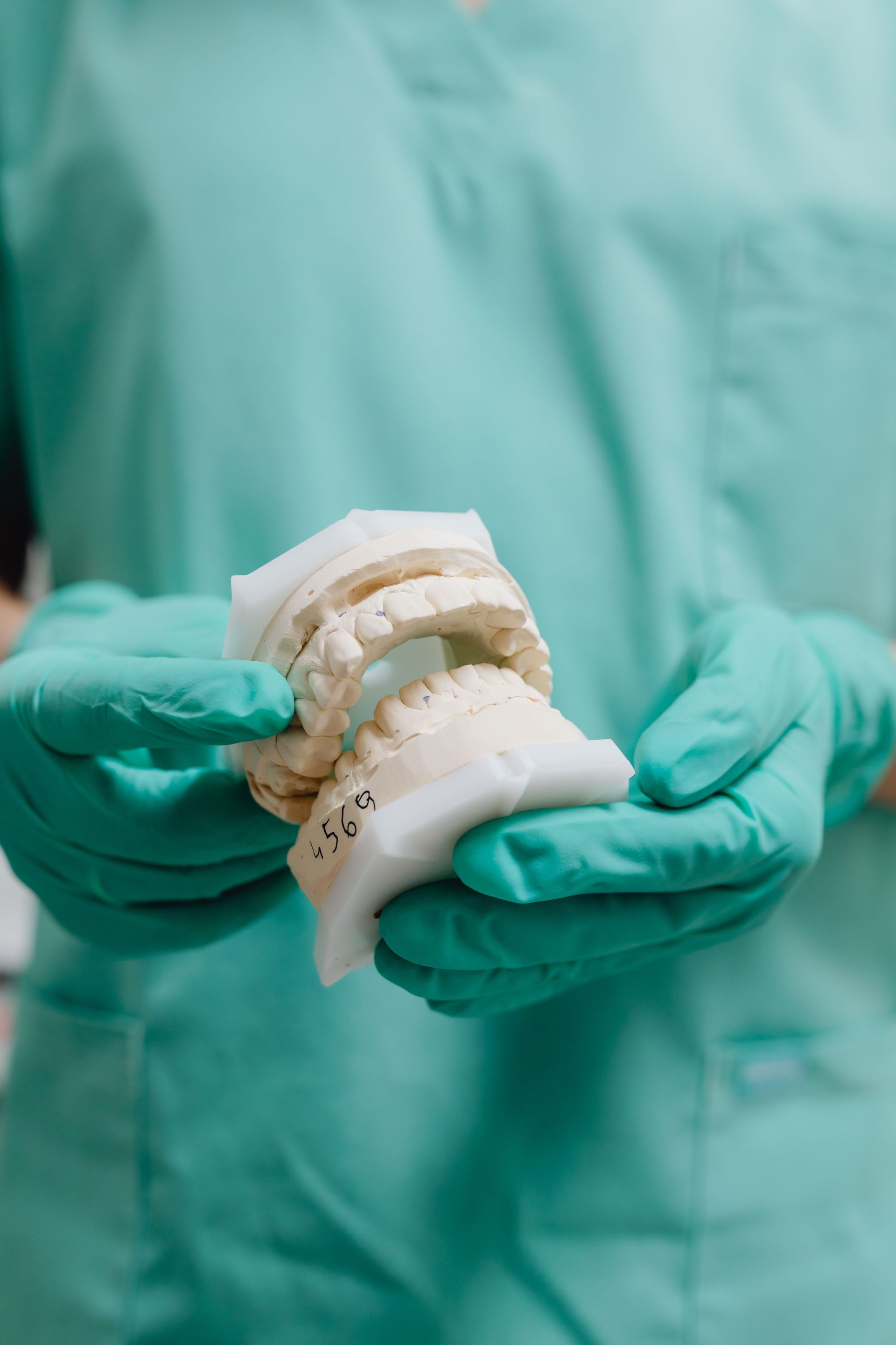 Manos enguantadas sosteniendo un modelo dental con dientes superiores e inferiores sobre un fondo de bata médica 
