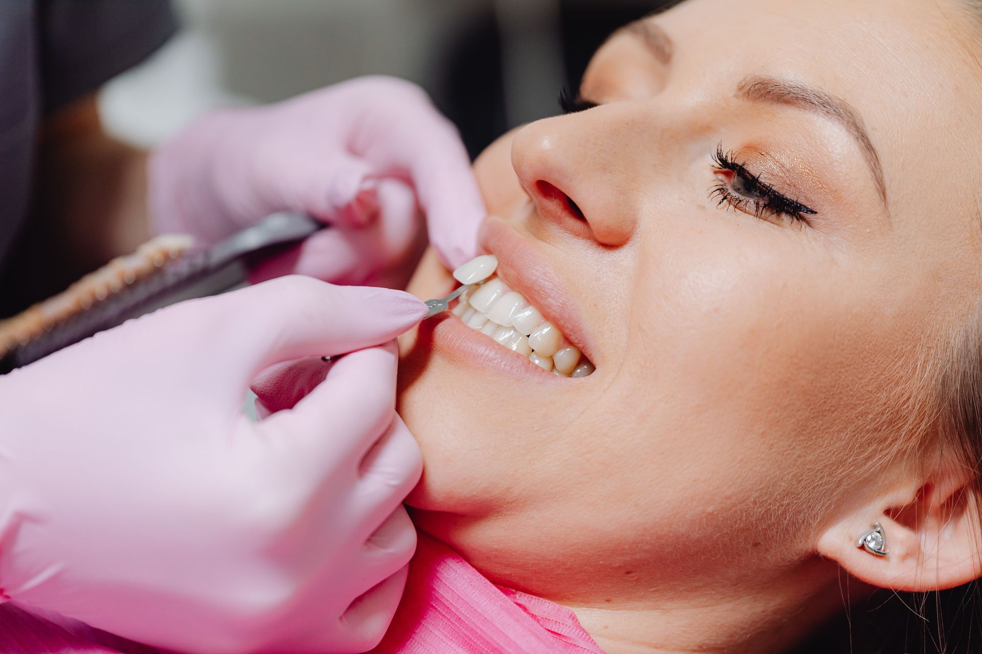 Un dentista ajusta los aparatos de ortodoncia de un paciente con las manos enguantadas de rosa.