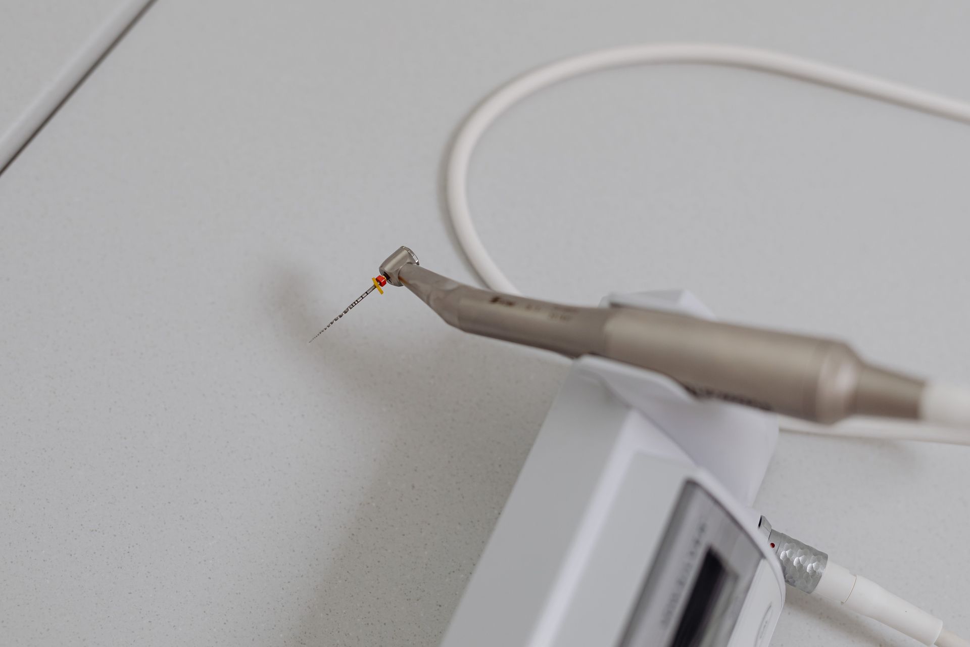Pinzas sujetando un pequeño insecto o un alambre sobre un enchufe de pared blanco y un cable.