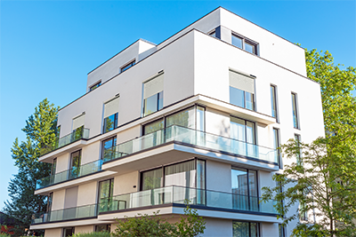 Ein modernes, weißes mehrstöckiges Wohnhaus mit Glasbalkonen, umgeben von Bäumen unter einem klaren blauen Himmel.