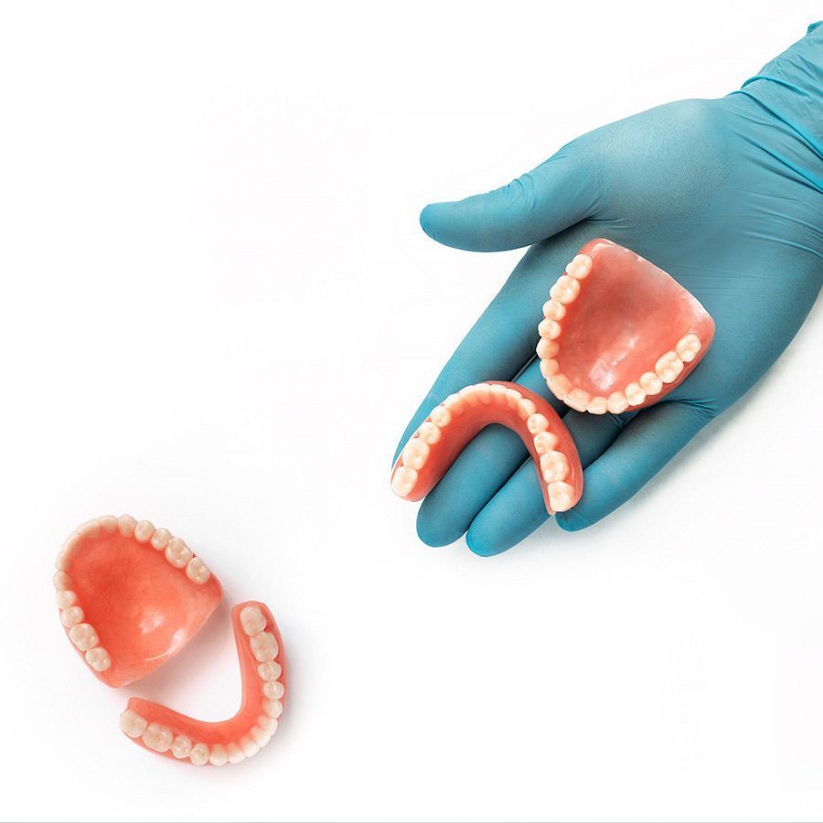 Una mano en un guante azul sostiene un par de dentaduras postizas.