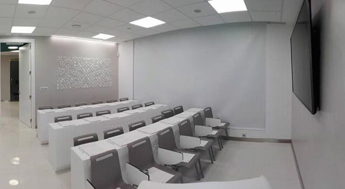 Un aula con filas de mesas y sillas y un televisor de pantalla plana en la pared.