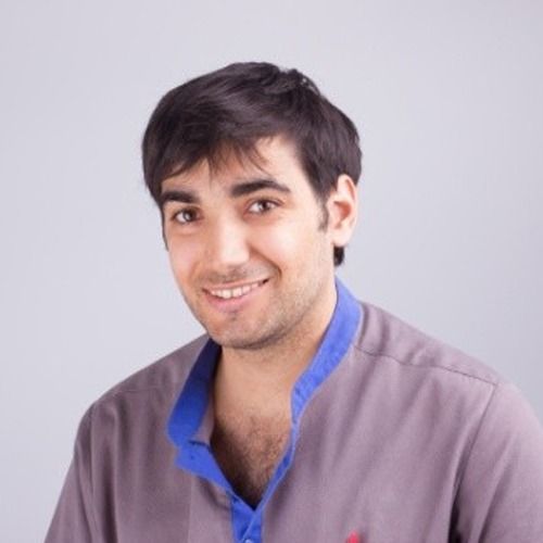 Un hombre con una camisa gris y cuello azul sonríe a la cámara.
