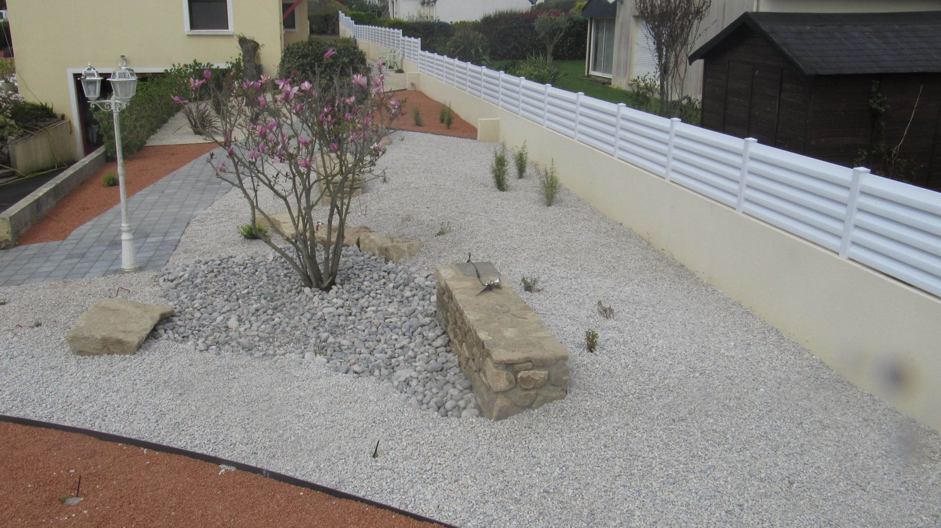 Aménagement extérieur en graviers, arbuste et banc en pierres