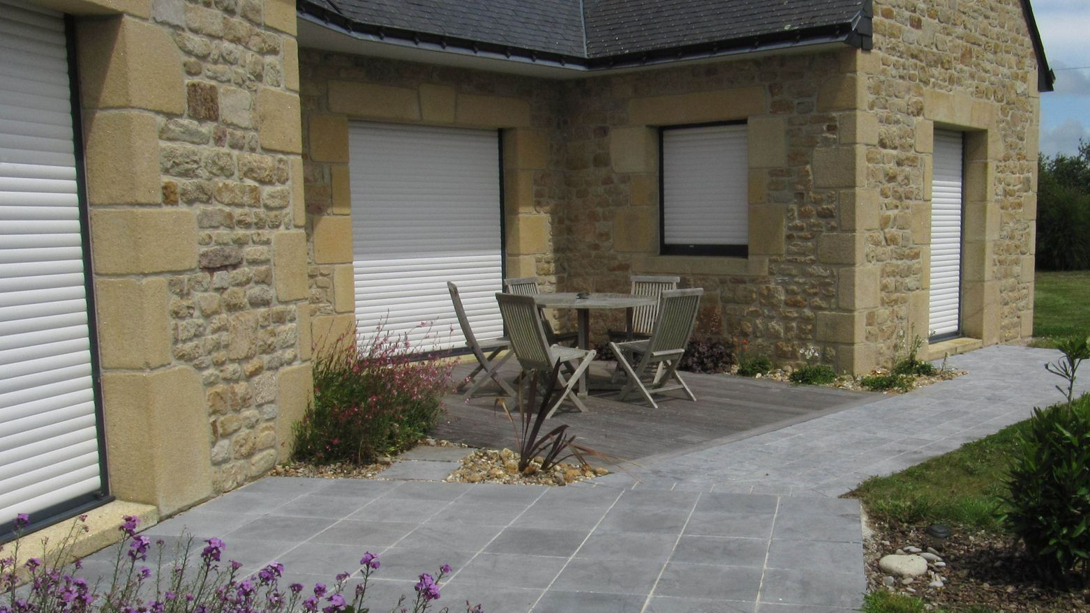 Une terrasse en pierres grises et carrées devant une maison bretonne
