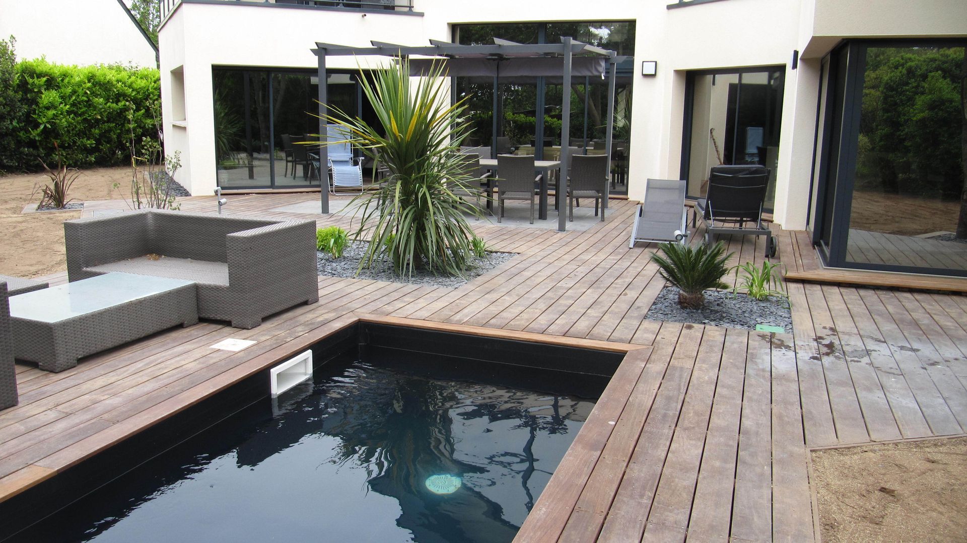 Une piscine au milieu d'une terrasse en bois et salon de jardin