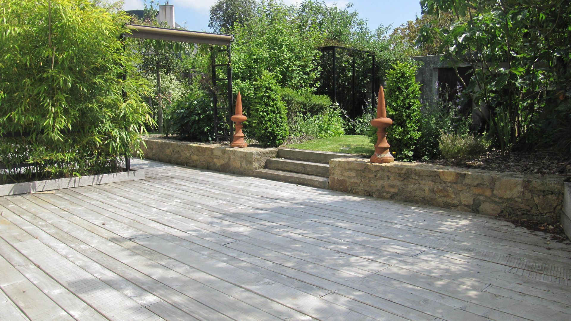 Grande terrasse en bois avec des arches et 3 marches vers le jardin