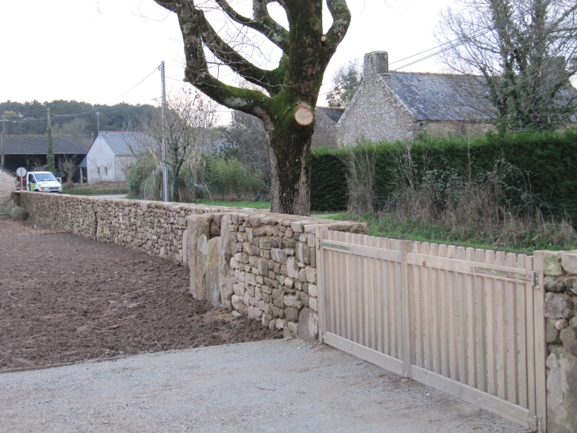 Un mur en pierres sèches et portail en bois et un arbre