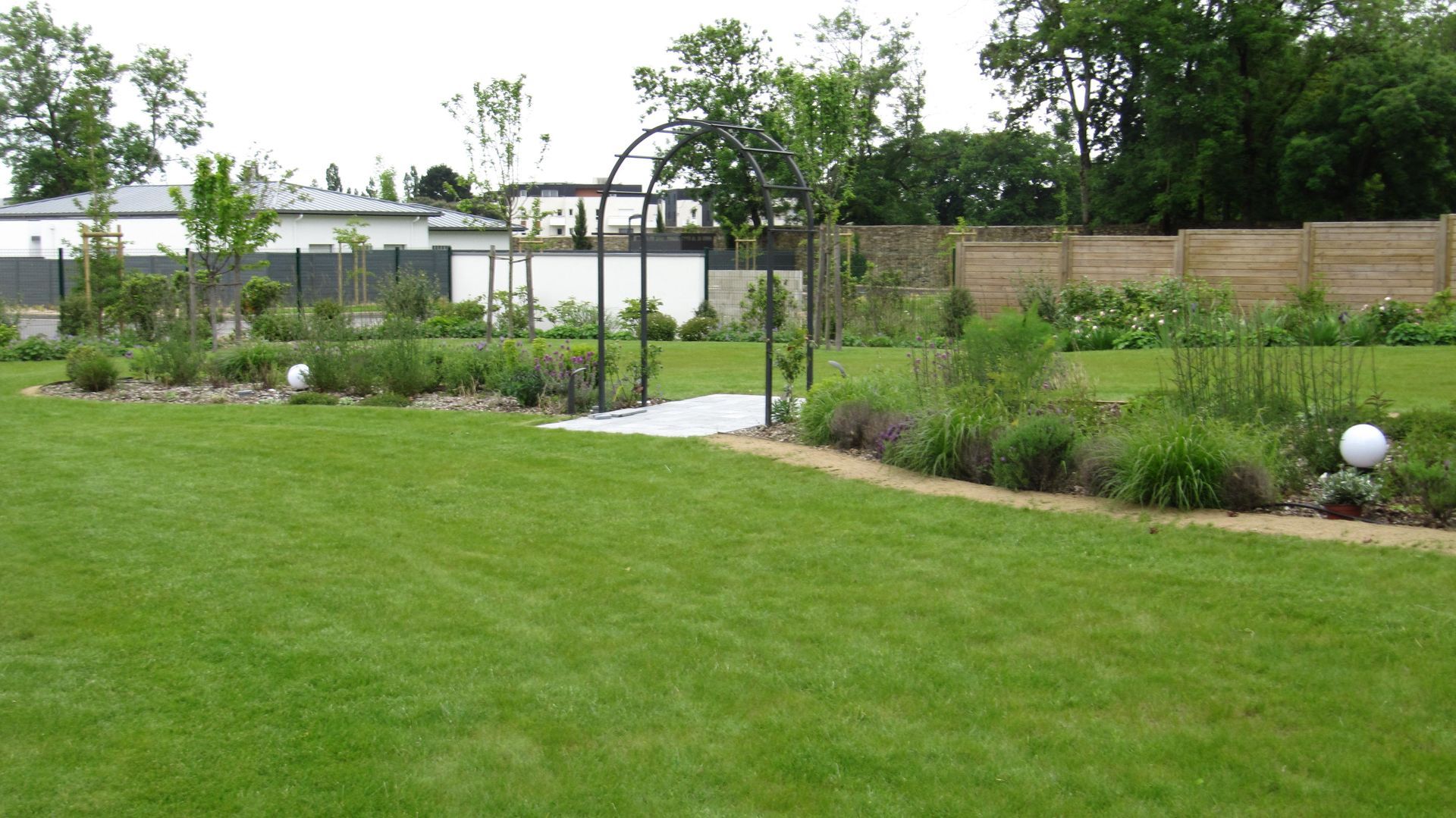 Gazon bien tondu, arche en métal et massifs