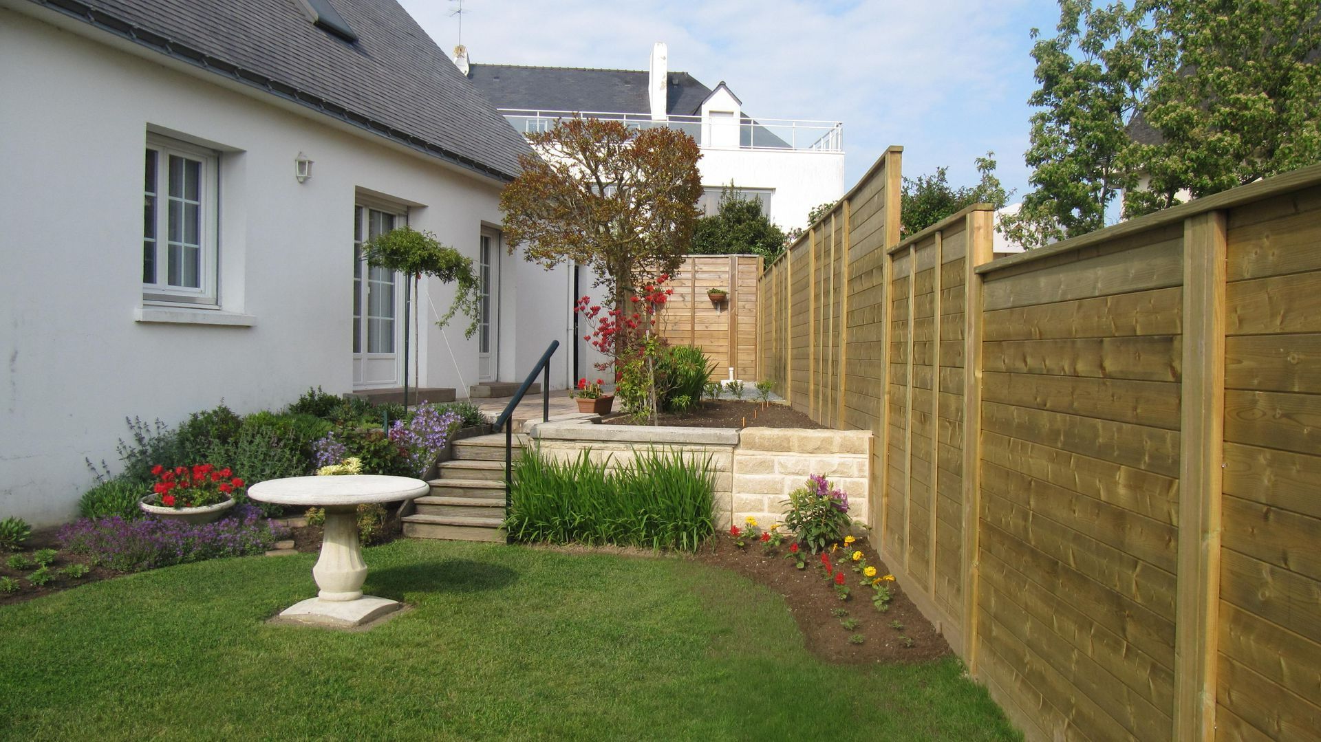 Jardin propre et entretenu, palissade en bois, terrasse et table en pierre