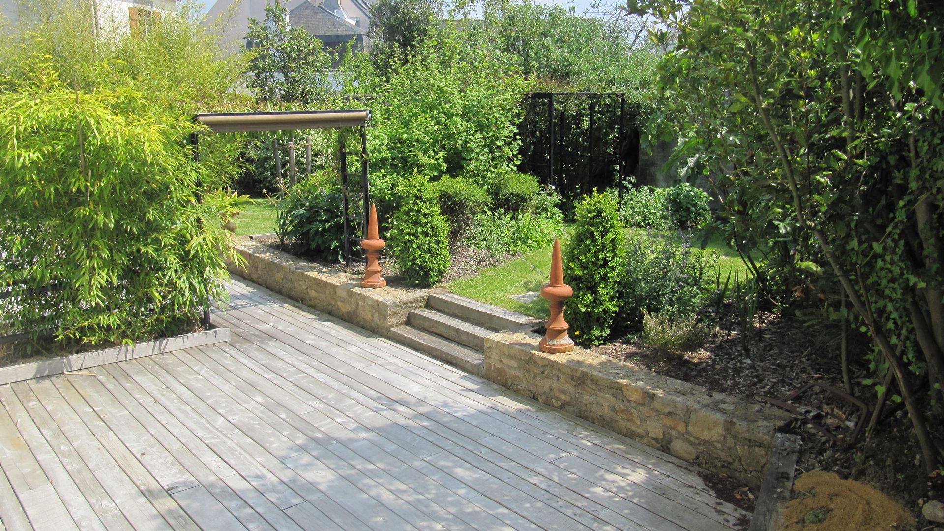 Terrasse en bois ombragée qui donne sur un jardin luxuriant et pergolas