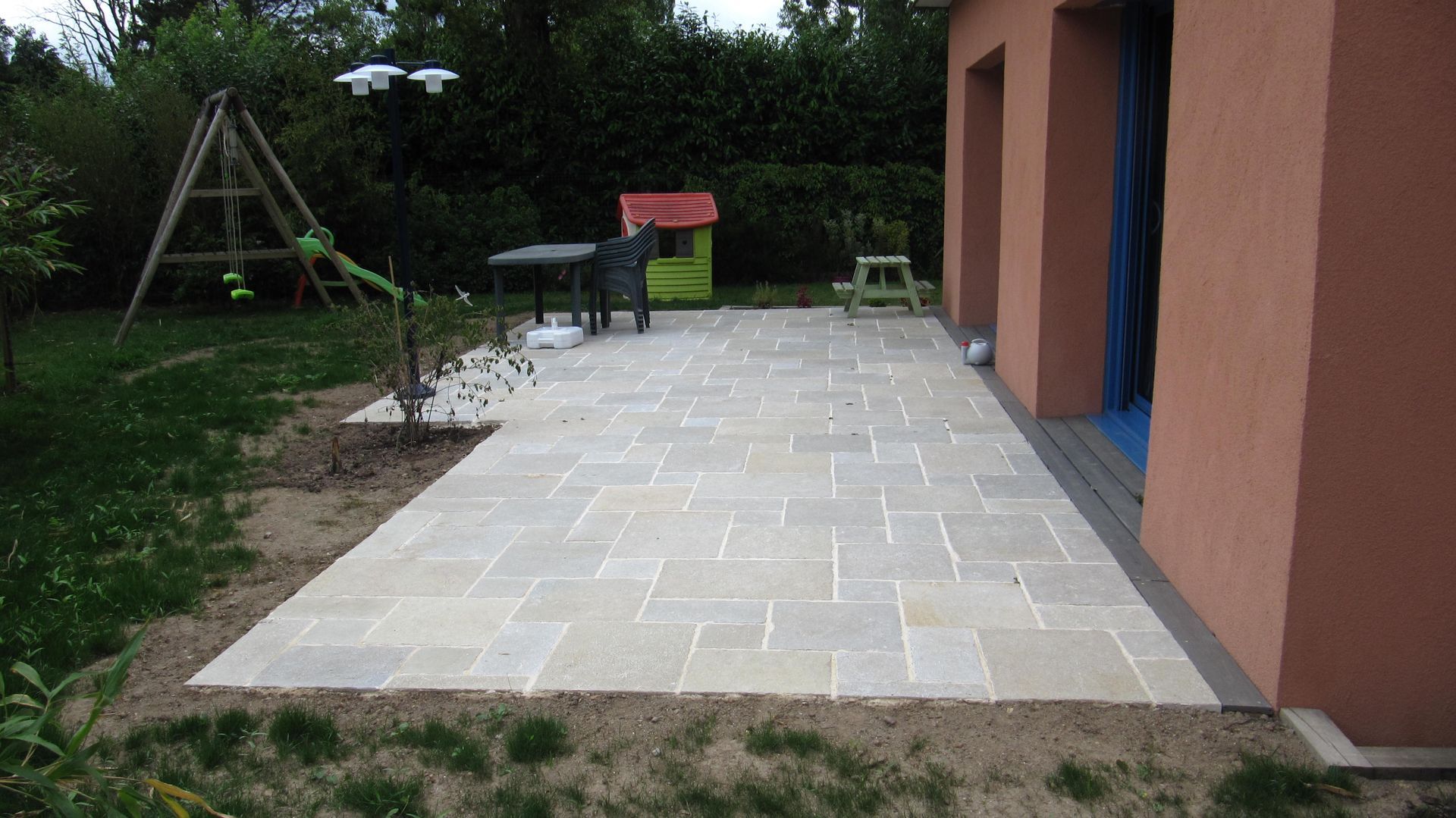 Une grande terrasse en pierres blanches avec des jeux pour enfants