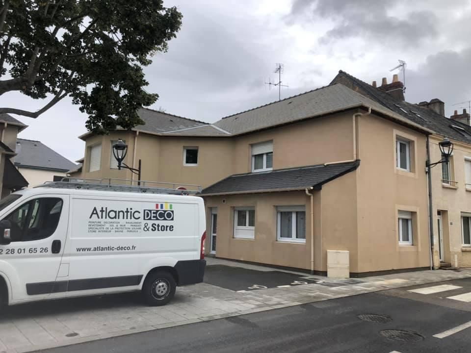 Une camionnette blanche de la marque Atlantic Deco & Store est garée devant un bâtiment beige de deux étages, dans une rue pavée.